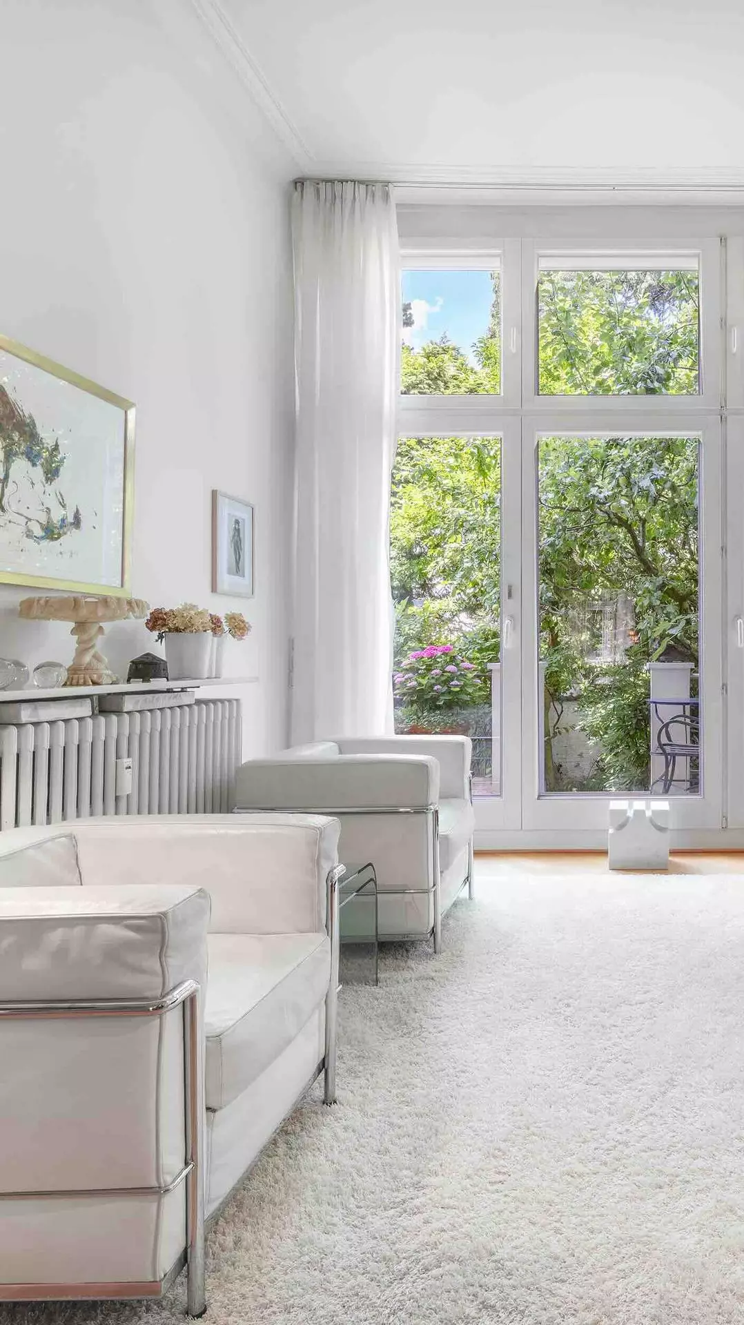Helles Altbau-Wohnzimmer mit weißen Designersesseln und bodentiefen Fenstern zum Garten